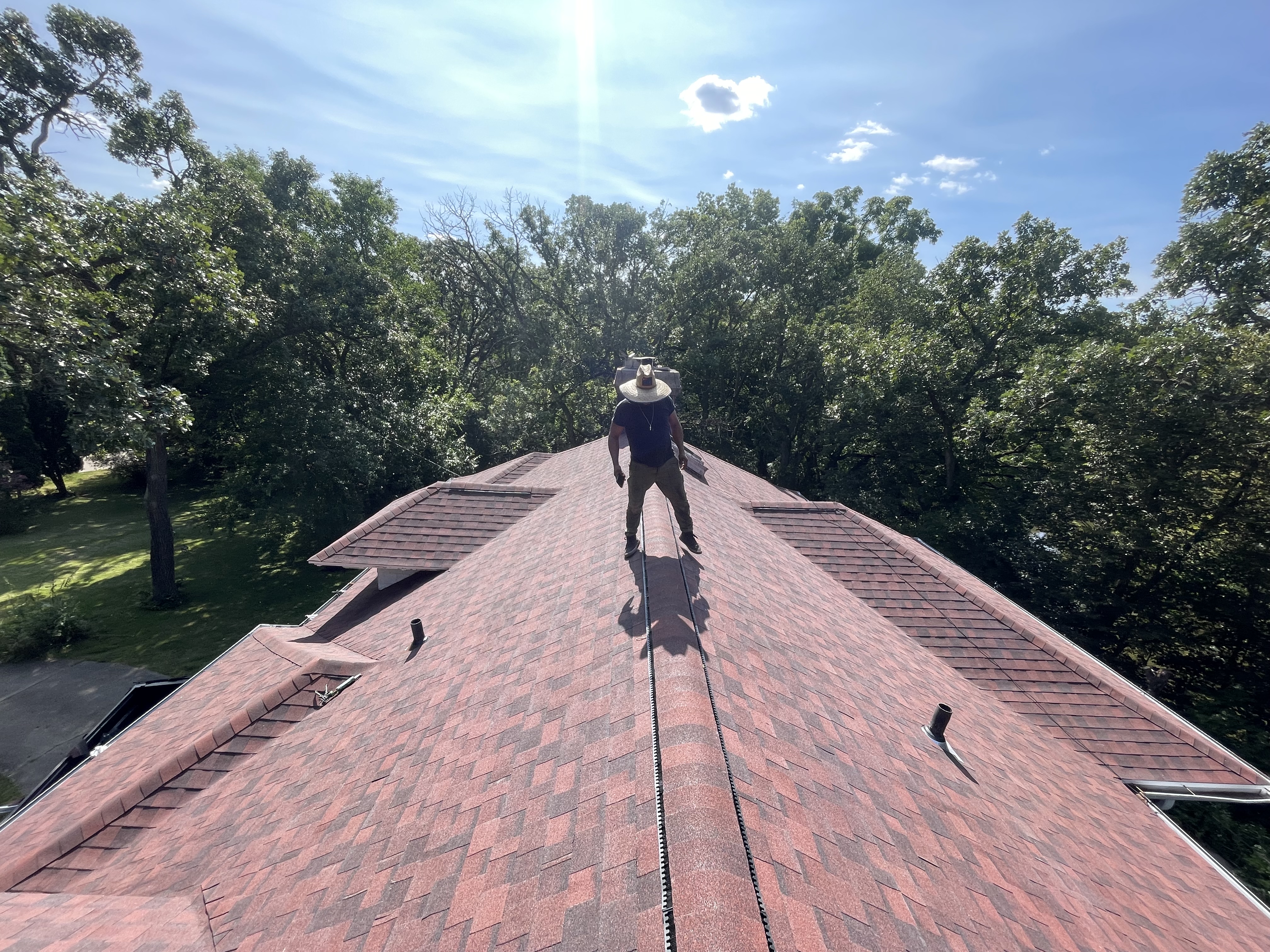 Pixler Construction roofer walking the ridge of a fresh red shingle roof